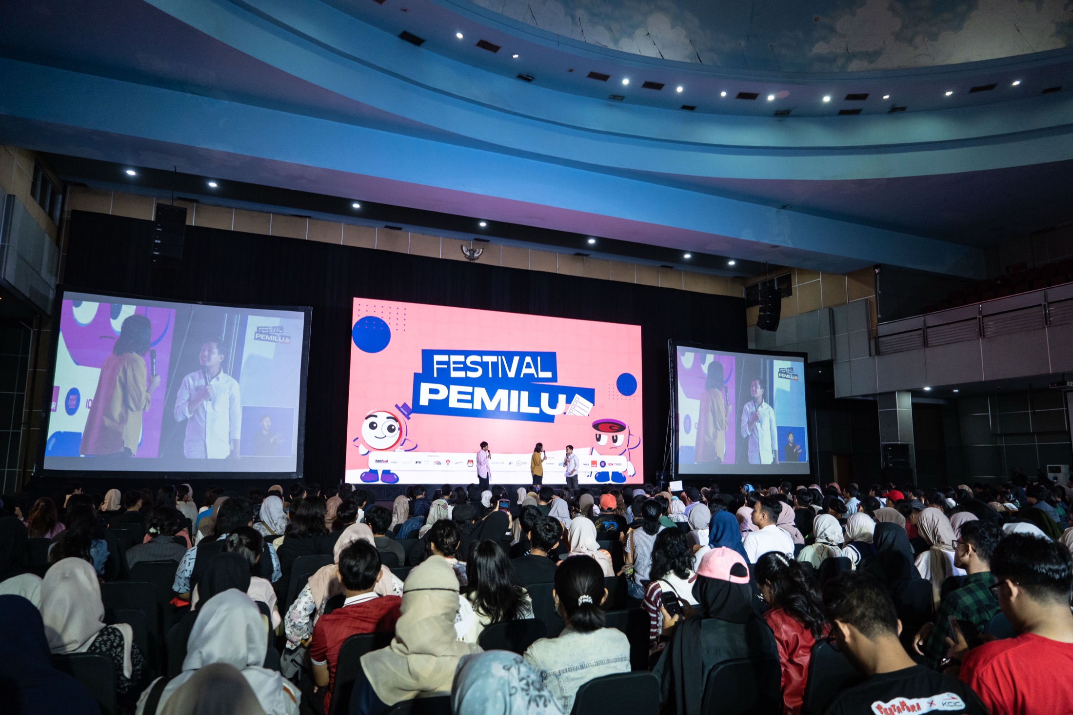 A full auditorium at Festival Pemilu 2024, with political party representatives on stage under a large Festival Pemilu screen
