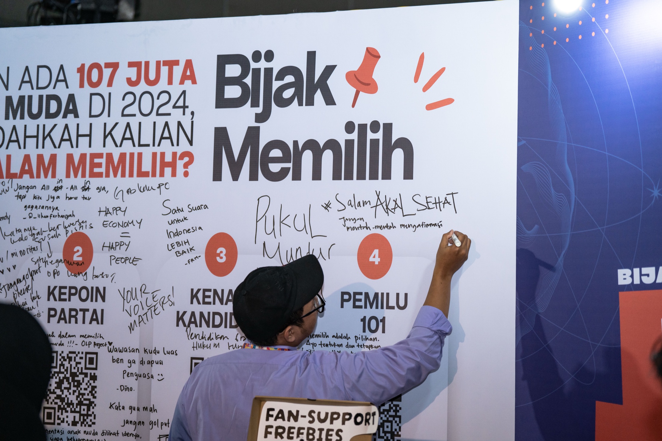 A visitor writing a message on the Bijak Memilih pledge wall